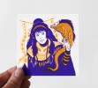 Photo d'une petite carte sérigraphié en deux couleurs, jaune et violet, représentant encore une fois une femme avec une tenue traditionnelle imaginaire, tenant dans sa main un lézard portant un masque.