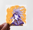 Photo d'une petite carte sérigraphié en deux couleurs, jaune et violet, représentant aussi une femme avec une tenue traditionnelle imaginaire, qui souffle de la fumée orange.